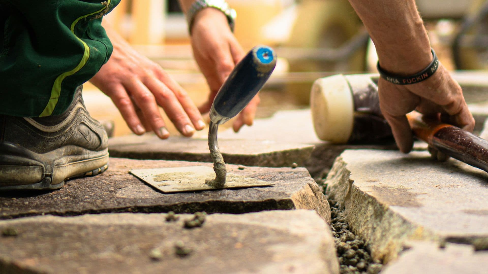 Two tradesmen's hands setting paving stones with a trowel