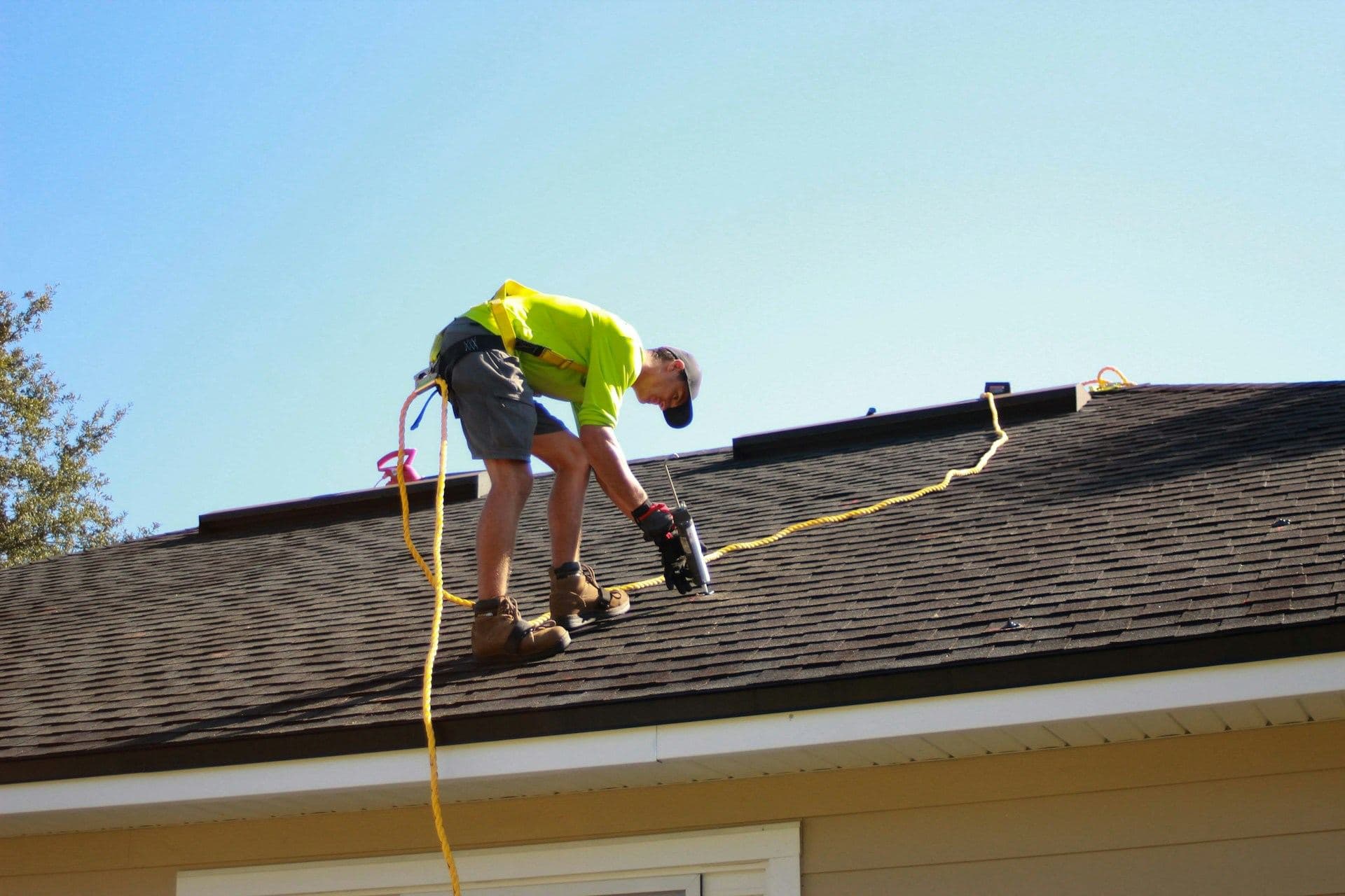 Roofer nailing shingles on a house roof on a clear day